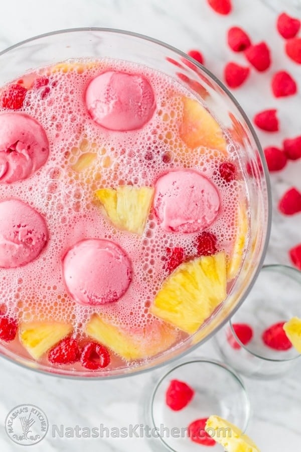 Pink-red punch bowl filled with raspberry punch, scoops of sherbet, and slices of pineapple and raspberries