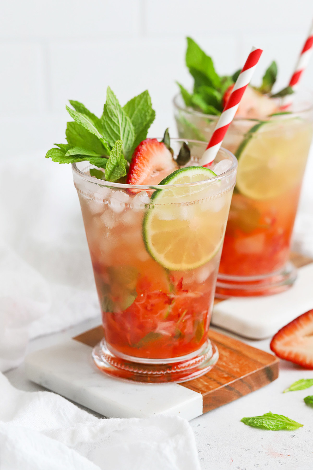 A full glass of crushed pebbly ice, thin lime slices, sliced strawberries, and strawberry mint julep