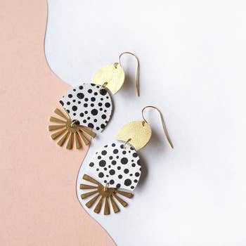 the earrings have a gold leather piece on top, connected to a black and white spotted piece, connected to a gold sunburst-shaped piece on the bottom 