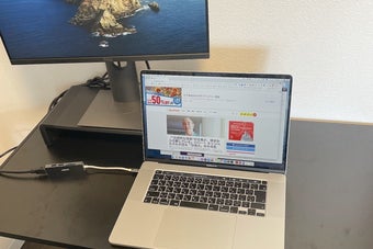 ノートパソコンの画面にニュース記事が表示されているデスク上のシンプルな作業スペース。電源や配線が整然と配置されている。