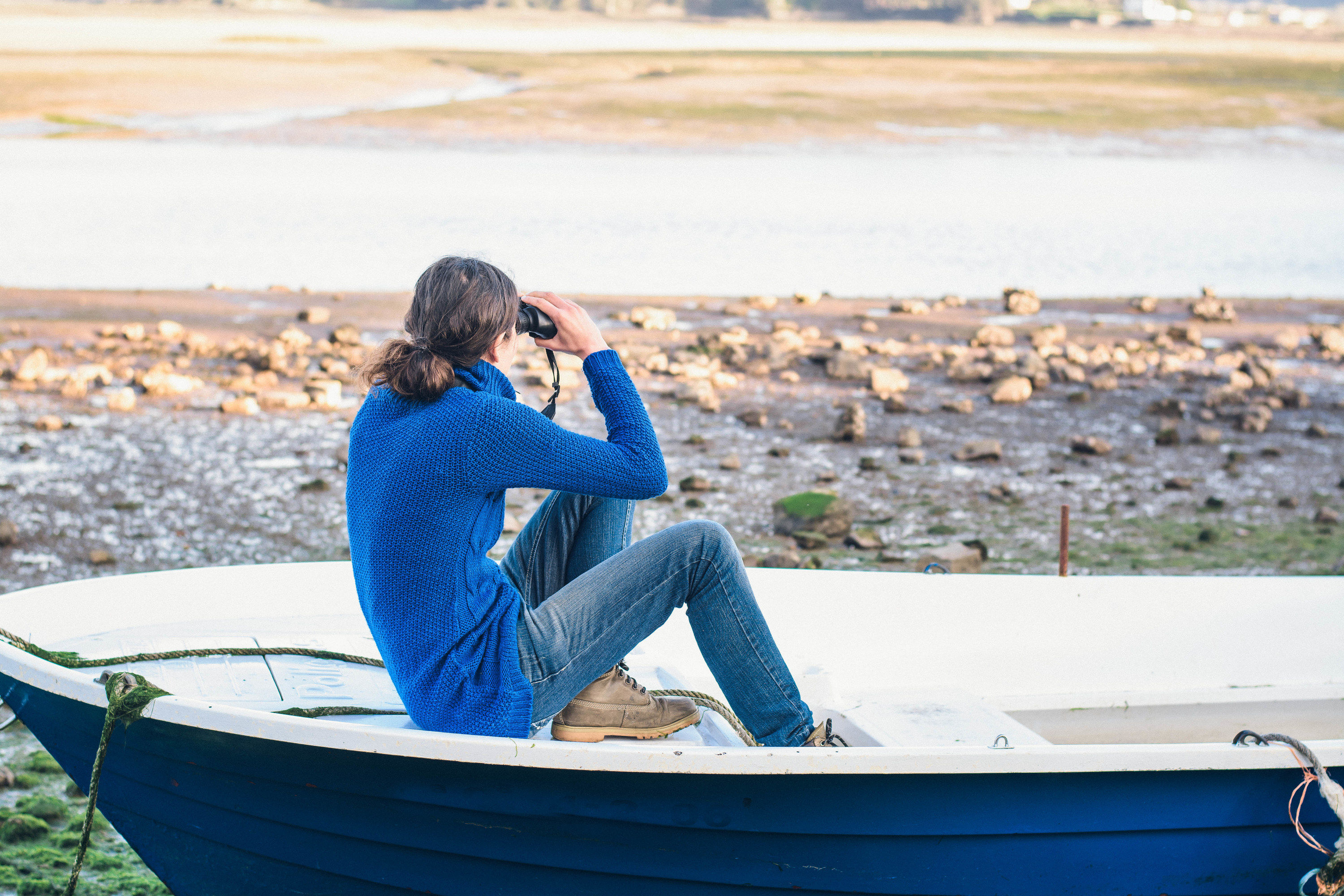 Photo of a woman in a blue boat looking through binoculars 