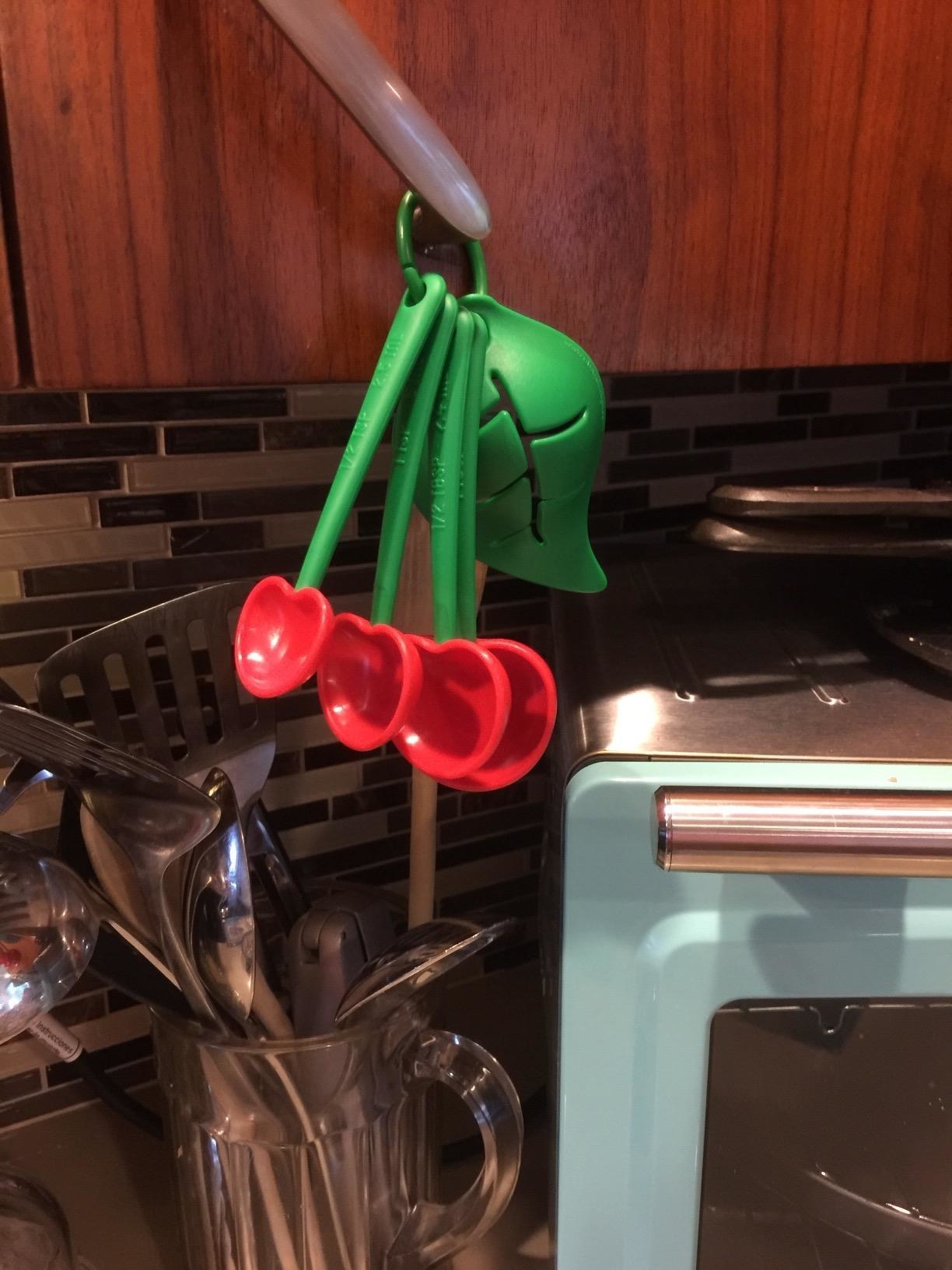 A reviewer photo of the measuring spoons, which have red, heart-shaped spoon surfaces and green handles