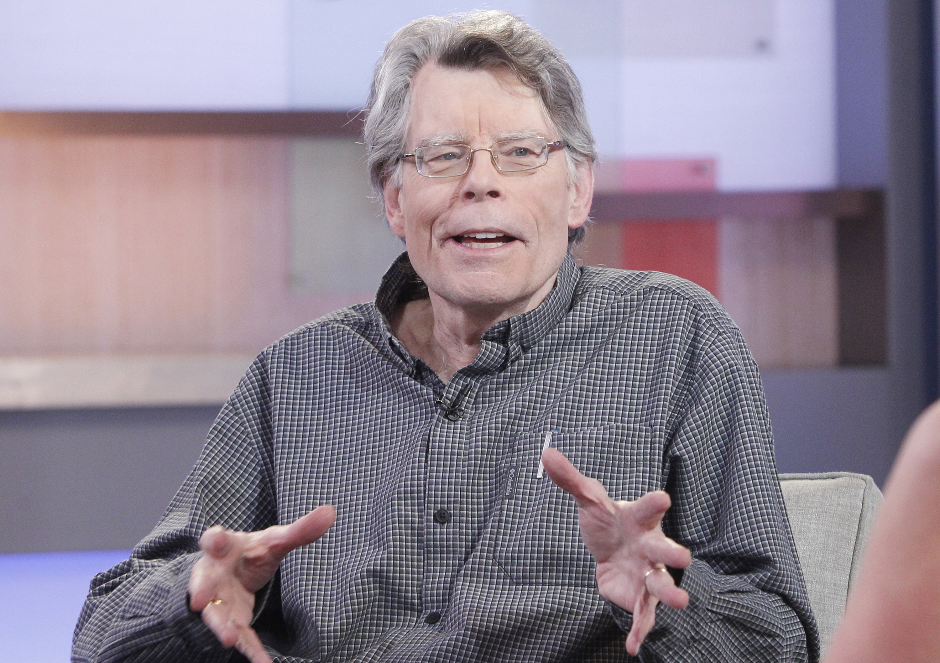 Stephen King talking to someone while sitting and gesturing with his hands