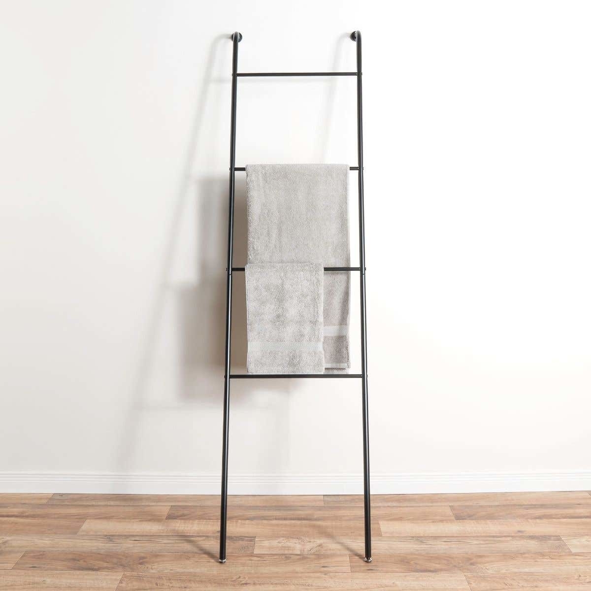 A ladder shelf leaning against a wall with towels hanging from it