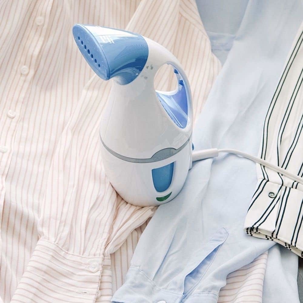 A handheld steamer on a pile of button up shirts