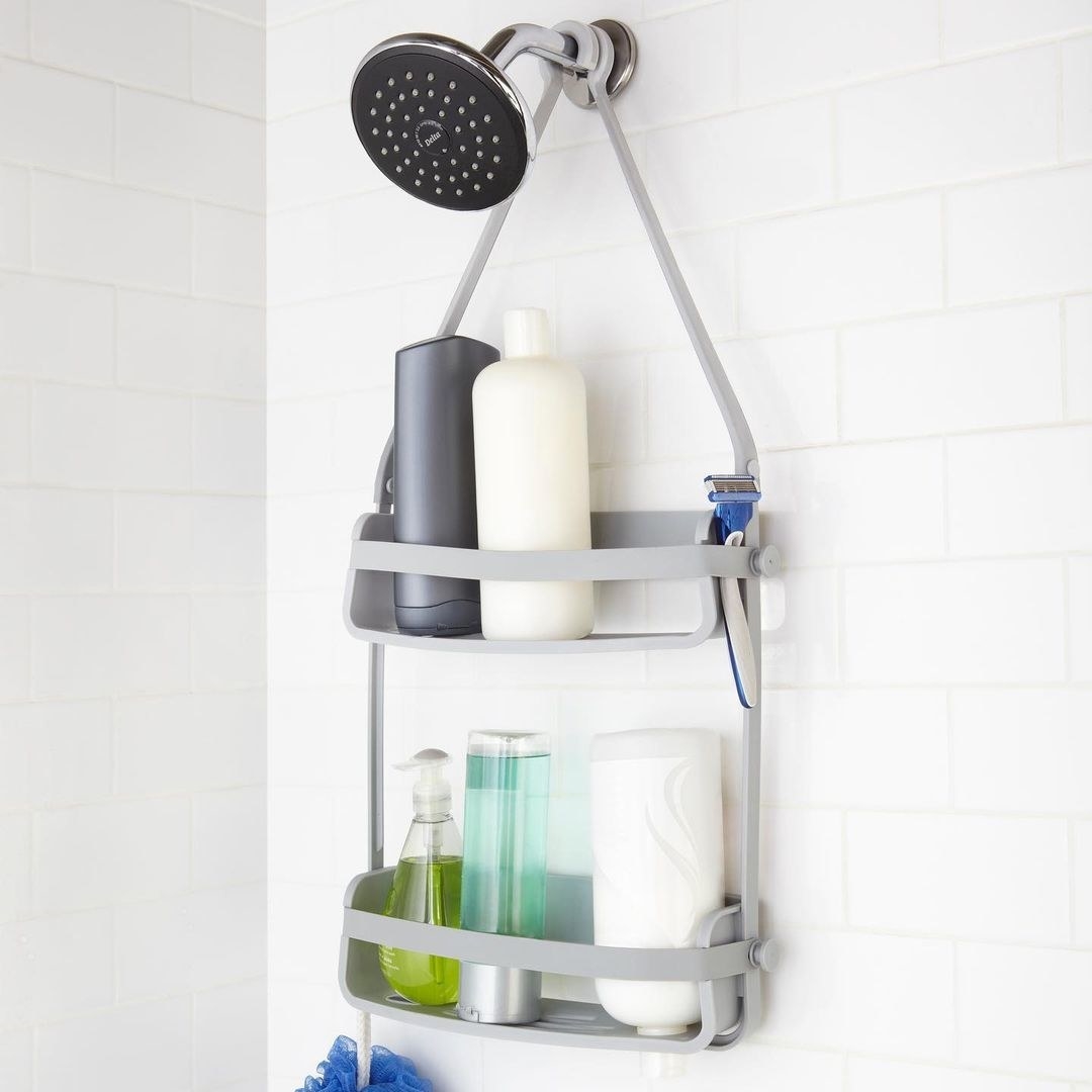 A two-tiered shower caddy filled with product and hanging from the showerhead 