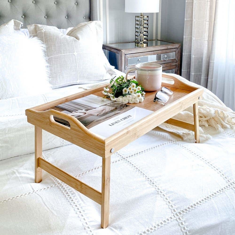 A wooden tray on a bed with a magazine on top