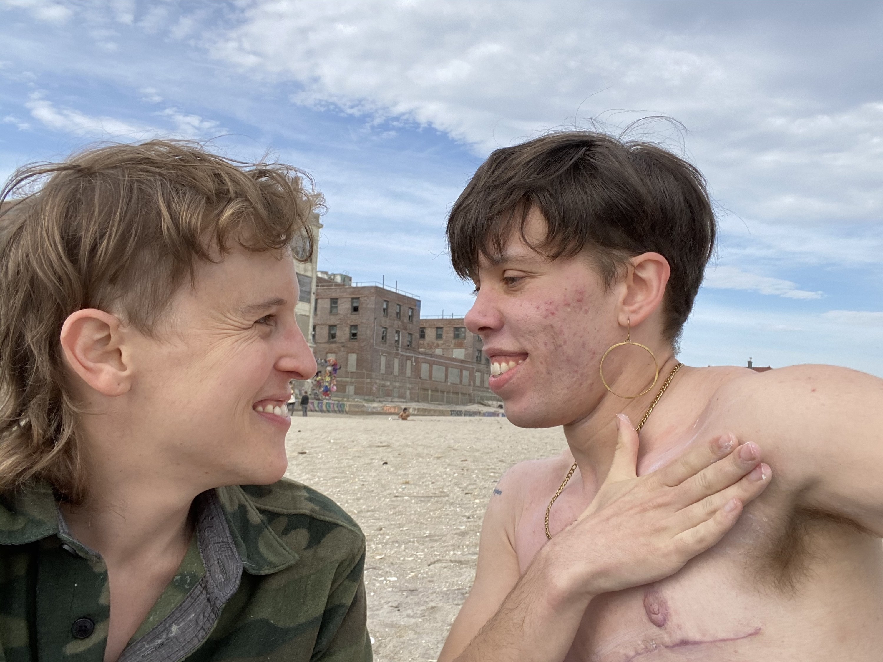 Two trans people smile at each other at Riis Beach, NYC