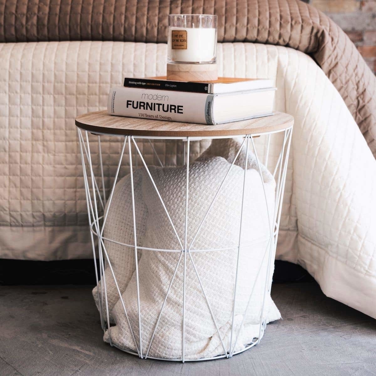 A large wiry metal basket with folded blankets and a wooden lid