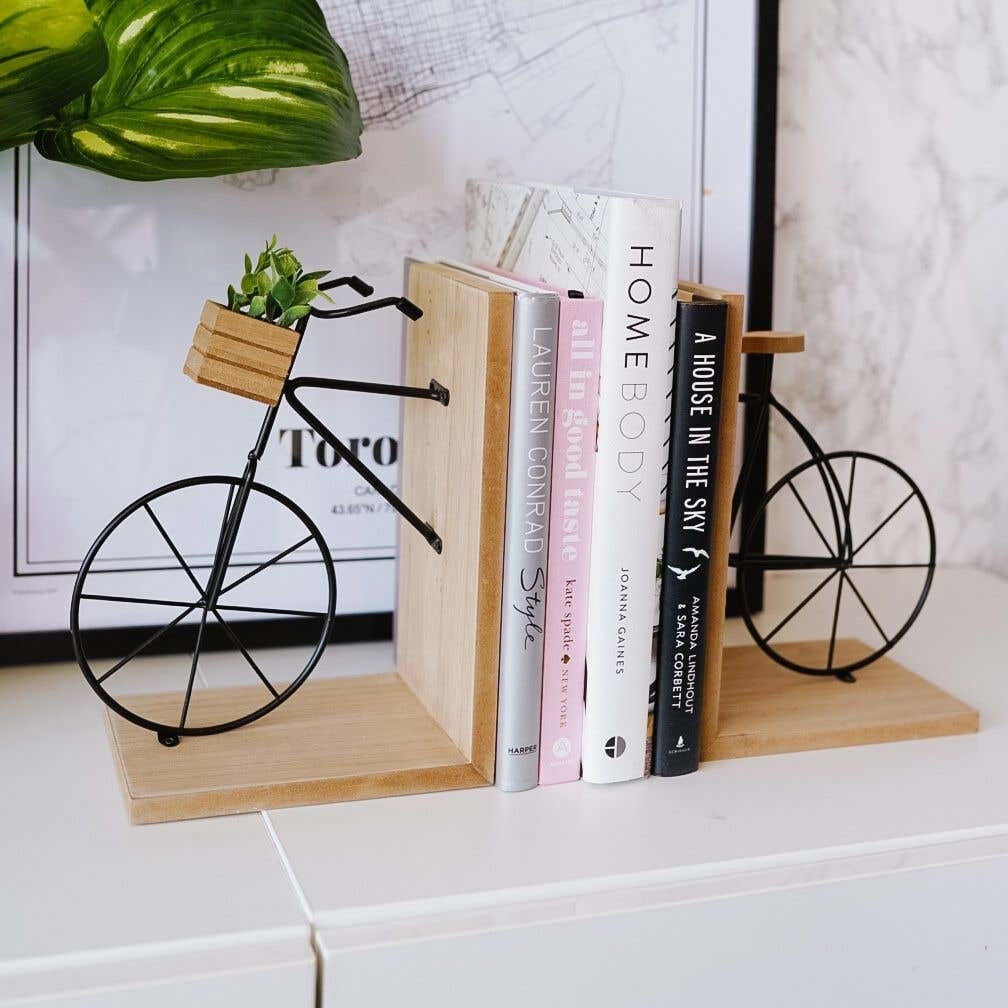 Four books stuck between two wooden bookends that look like the front and back of a bike