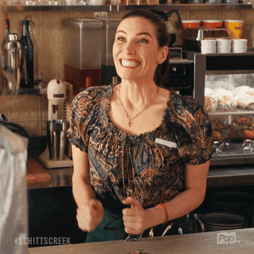 Twyla from &quot;Schitt&#x27;s Creek,&quot; excited behind the counter of her restaurant.