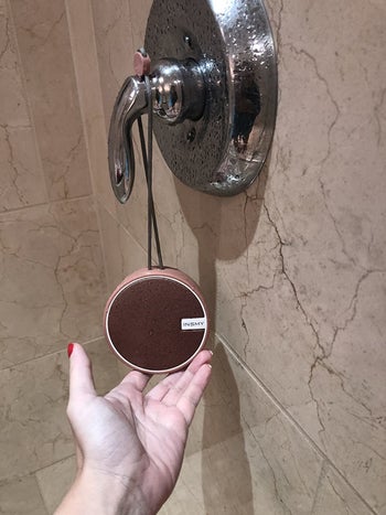 Reviewer holding shower speaker hanging on shower handle
