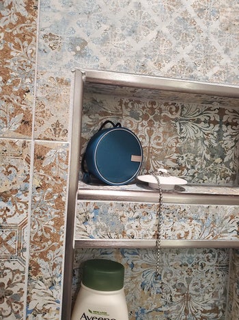 Reviewer's shower shelf with waterproof speaker placed on top