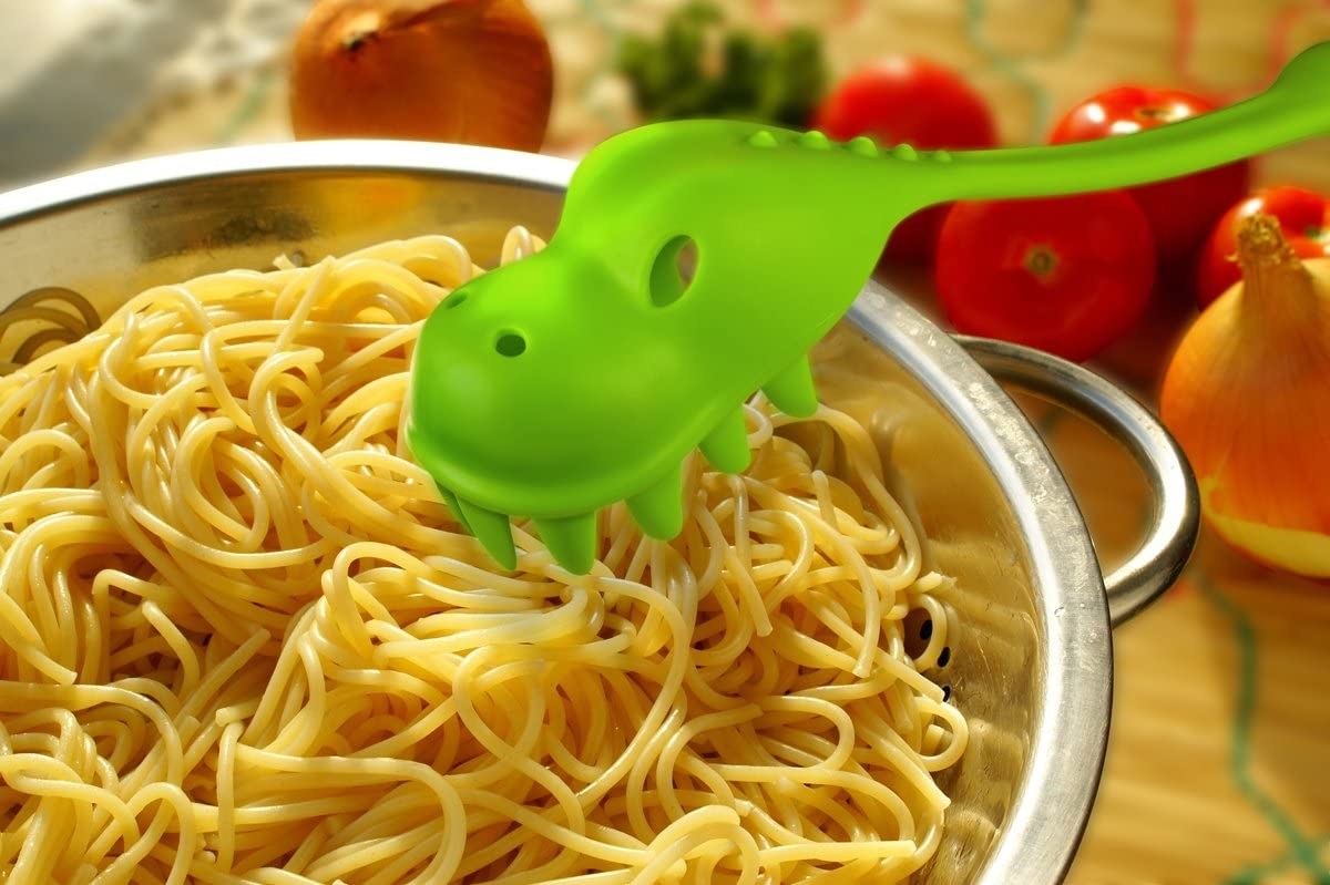 Dinosaur-shaped pasta server sitting over bowl of pasta