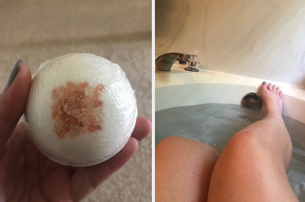 Hand holding a bath bomb next to legs in a tub