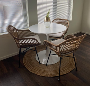reviewer's chairs made of light tan weaving rattan material with a square-ish shape and black, metal legs. They're at a white tulip table with a woven circular 