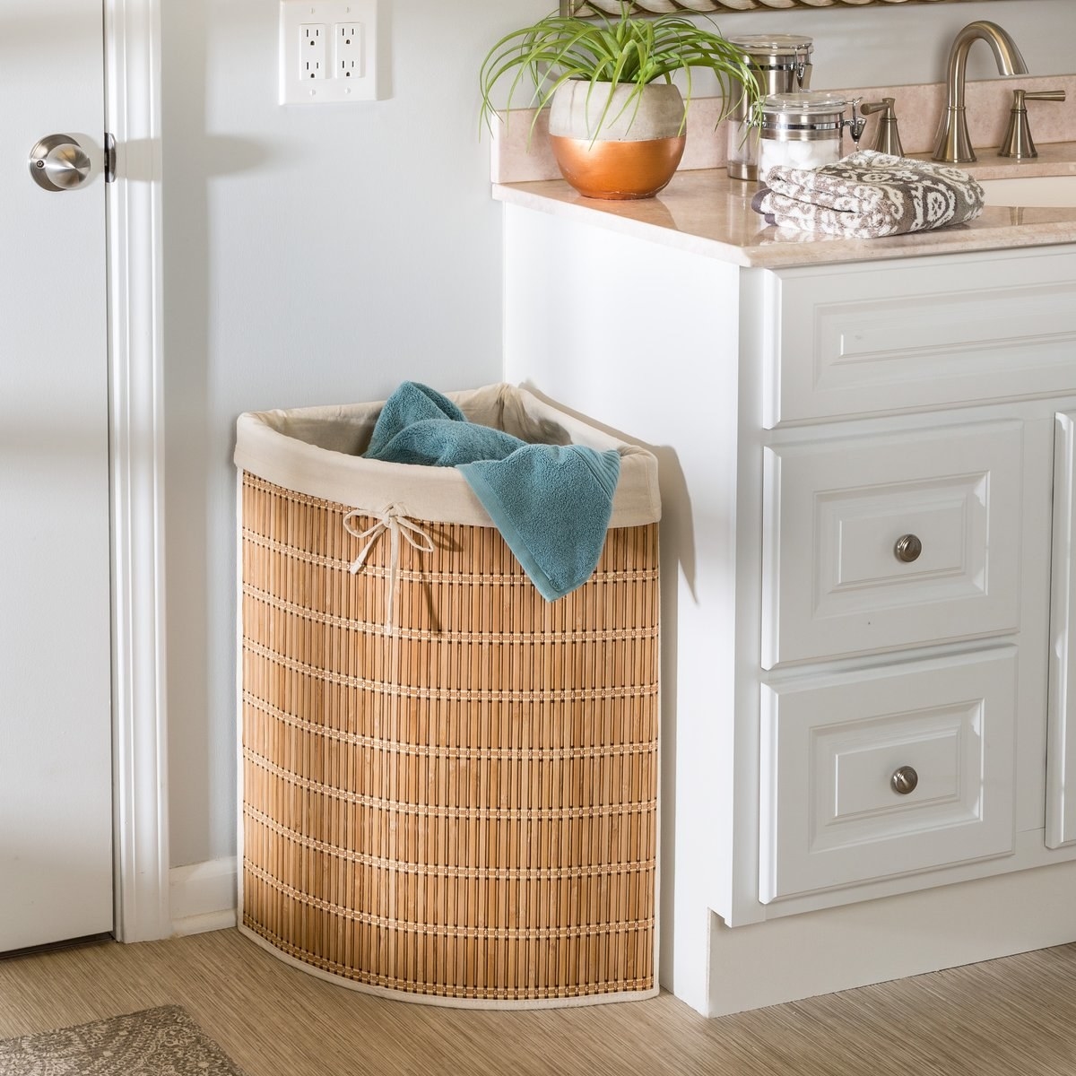 The laundry hamper with a towel in it, set in the corner of a room next to a countertop and a door