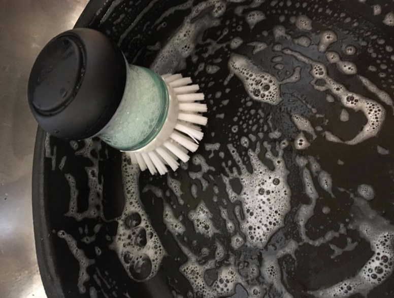 A reviewer&#x27;s scrub brush with suds in a pan