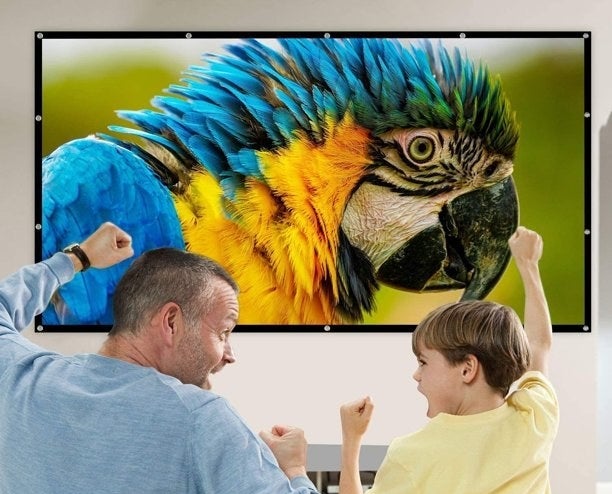 two model cheering while they sit in front of the mounted projector screen with a parrot being projected onto it 