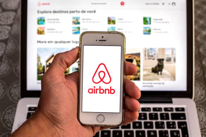 the Airbnb app seen displayed on a smartphone screen with the Airbnb website displayed on a laptop in the background