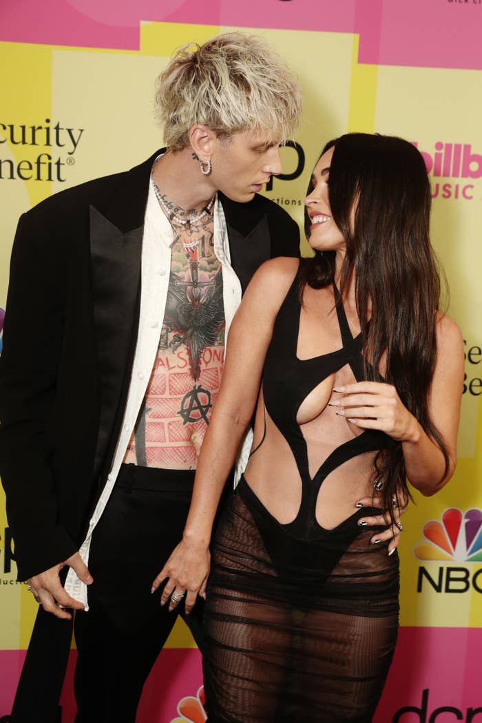 Megan looks back and smiles at MGK on the carpet while wearing a sheer skirt and cutout top