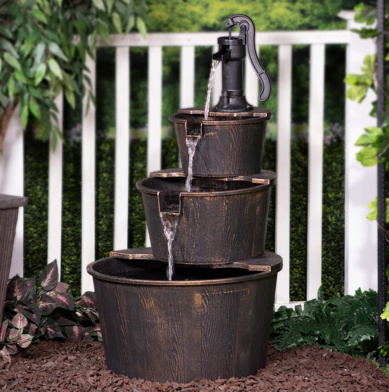 a three-tier water fountain sitting in a garden with a vintage pump top 