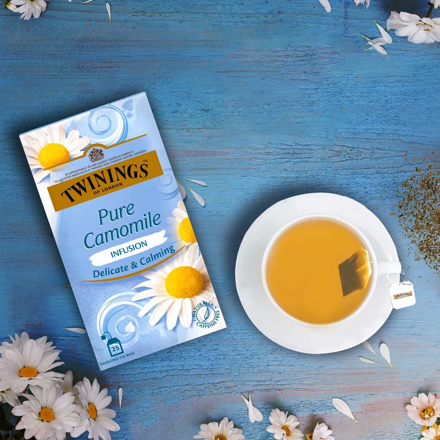 The pack of tea pictured with a cup of camomile tea and camomile flowers