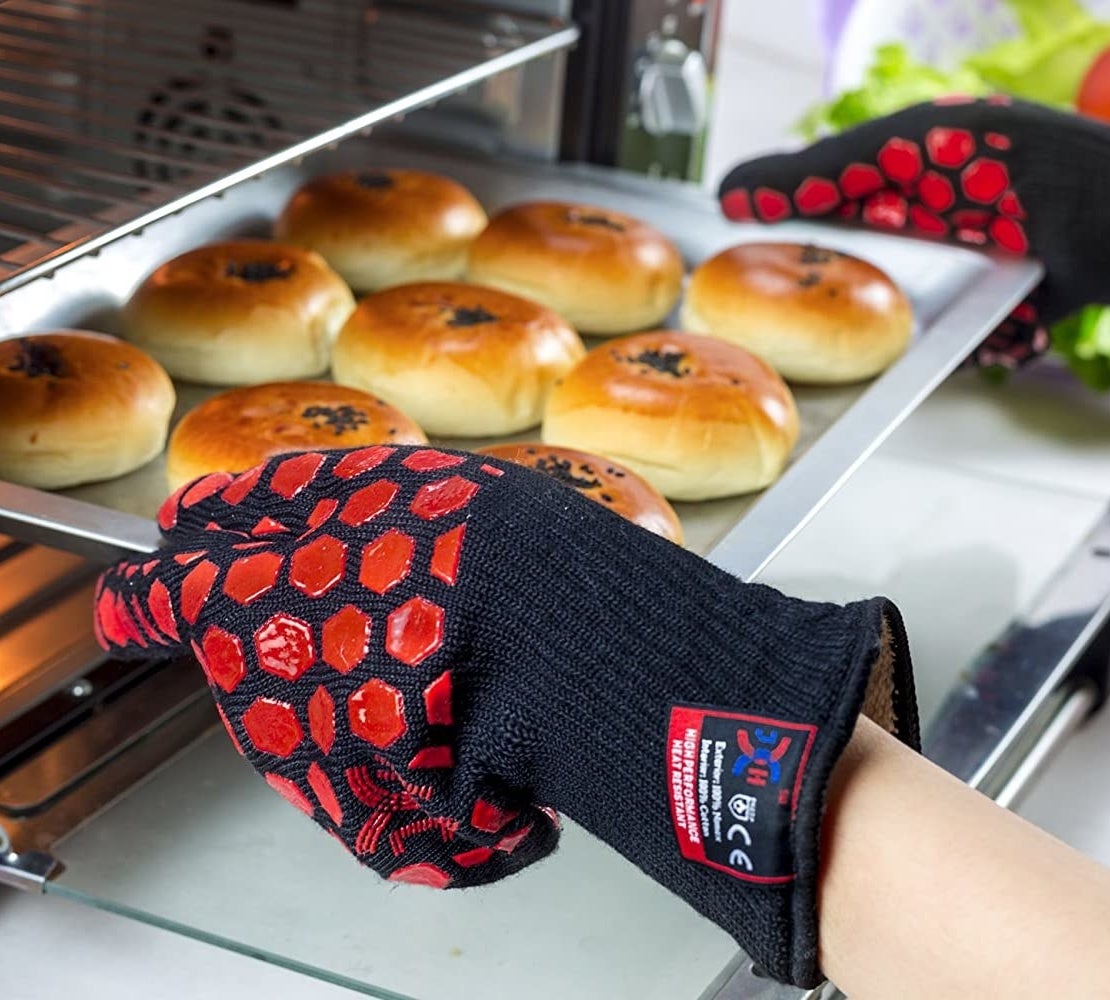 A person wearing the gloves while taking buns out of an oven