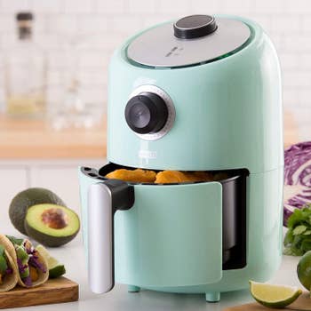 A small light blue air fryer with the basket open to show tater tots 