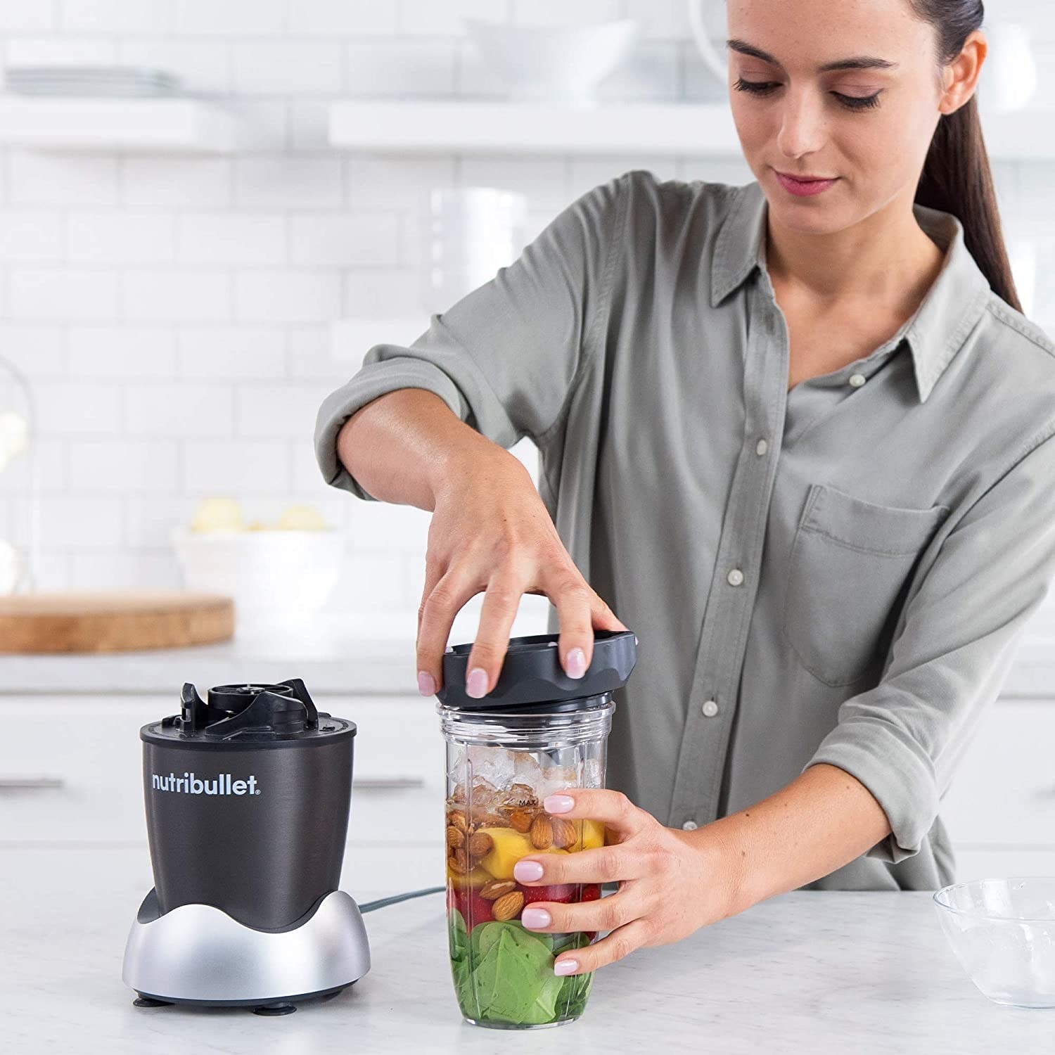 a model fastens a lid onto the nutribullet blender, which is full of almonds, spinach, and fruits