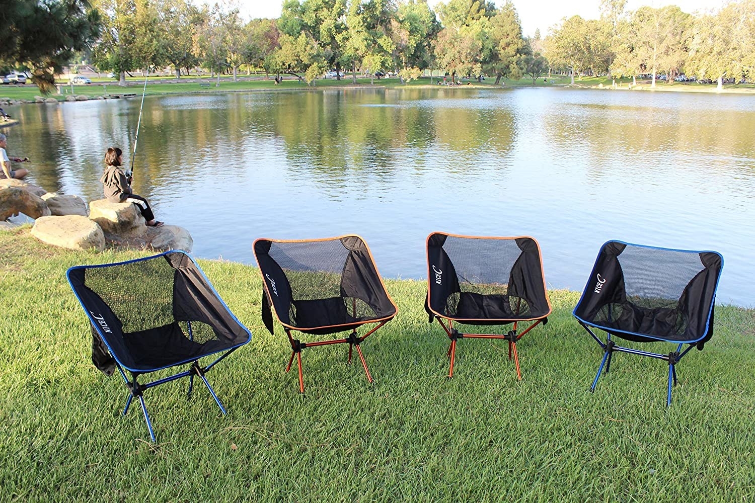 A row of four portable camping chairs by a lake