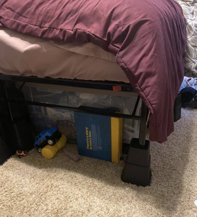 Reviewer lifting blanket to show items stored under a bed raises by the black bed risers 