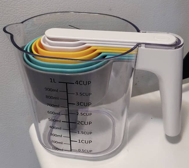 Clear four cup measuring cup with other cups and spoons nested inside it in yellow, gray, blue, and white 