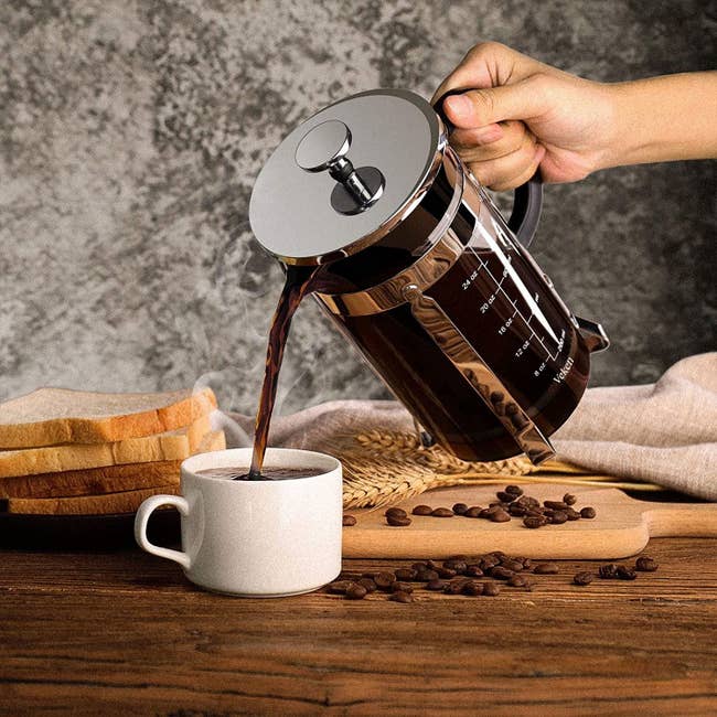 Model pouring coffee from a clear glass french press with a metal lid and handle 