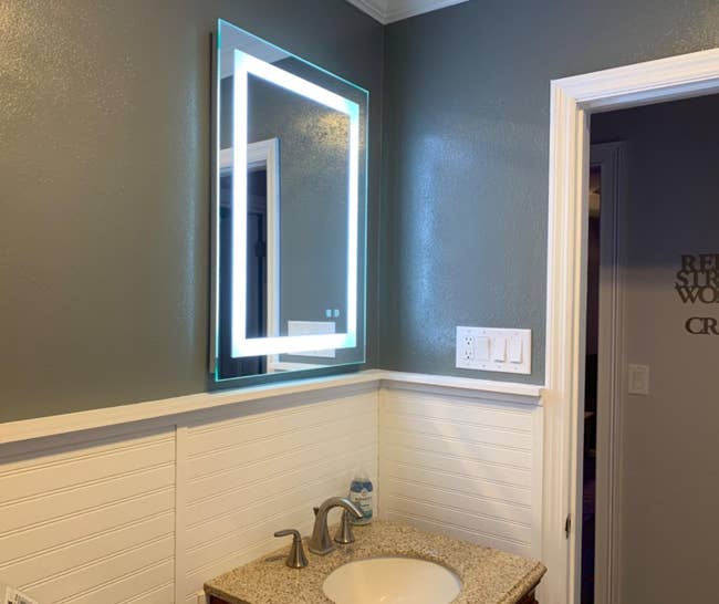 The mirror with a square-shaped perimeter of LED lights hanging over a bathroom sink
