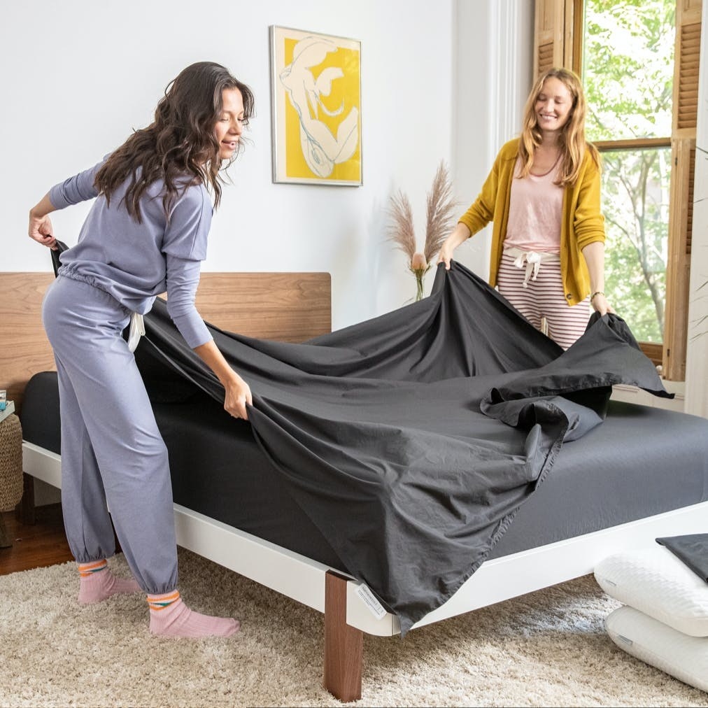 Two models putting black percale sheet set on bed 