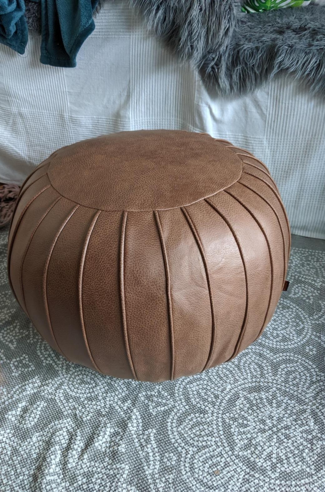 The brown circular pouf with a vertical line pattern around the entire thing 
