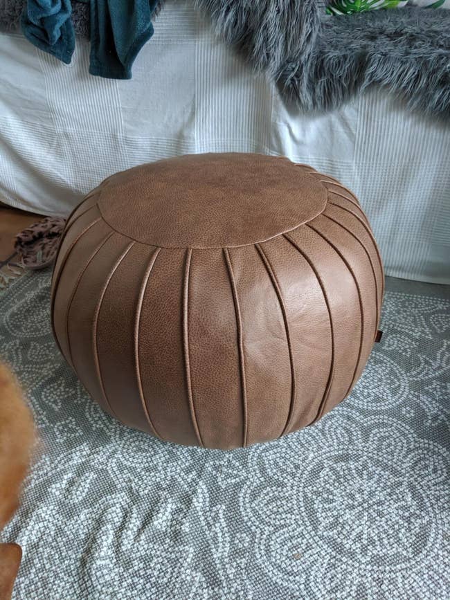 The brown circular pouf with a vertical line pattern around the entire thing 