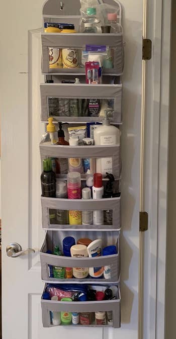Reviewer image of gray six shelf fabric organizer hung on door full of bathroom products 