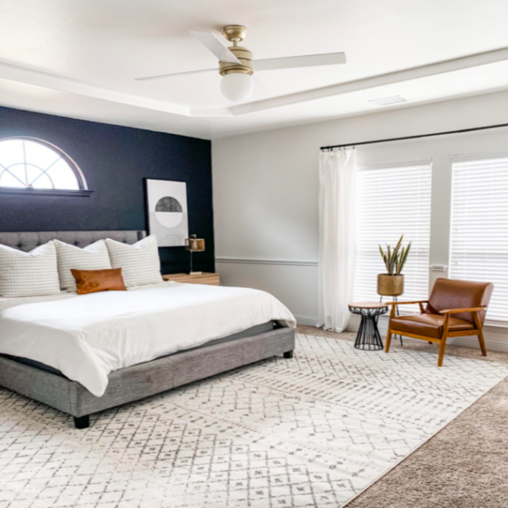 white duvet with three white pillows, a white textured rug, and a rattan accent chair