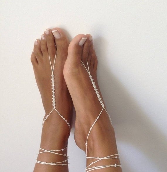 a model wearing beaded barefoot sandals with multiple bands wrapped around the ankles 
