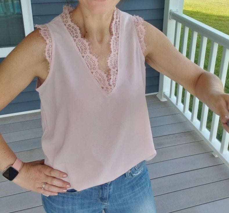 A reviewer wearing the pink v-neck, lace-trimmed tank with a pair of jeans