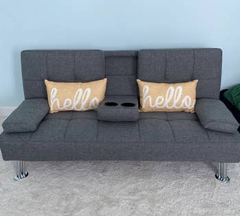 Small gray tufted couch with arm rests and a drink holder that comes down in the middle 