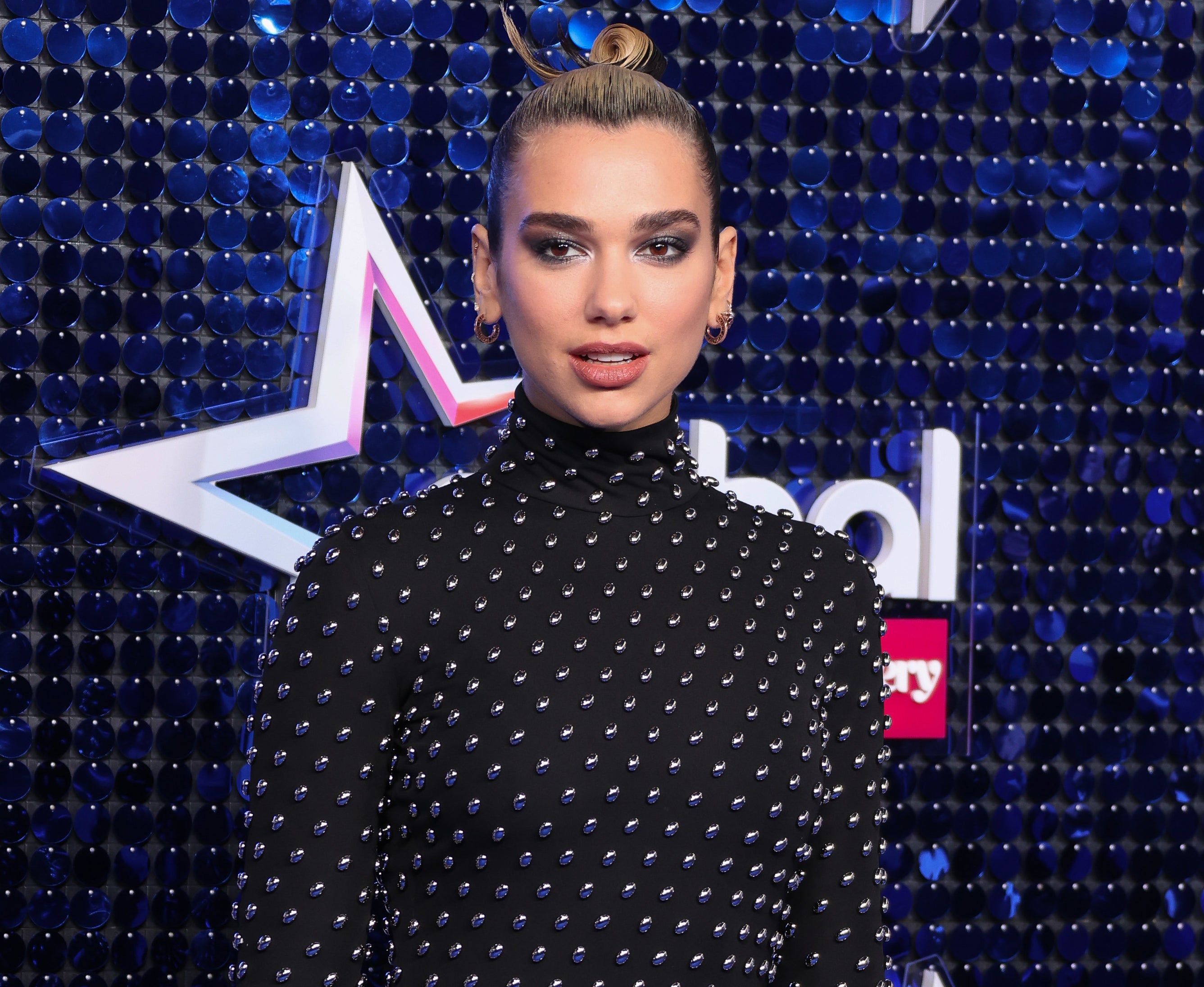 Dua looks serious in a black long-sleeve dress at an event