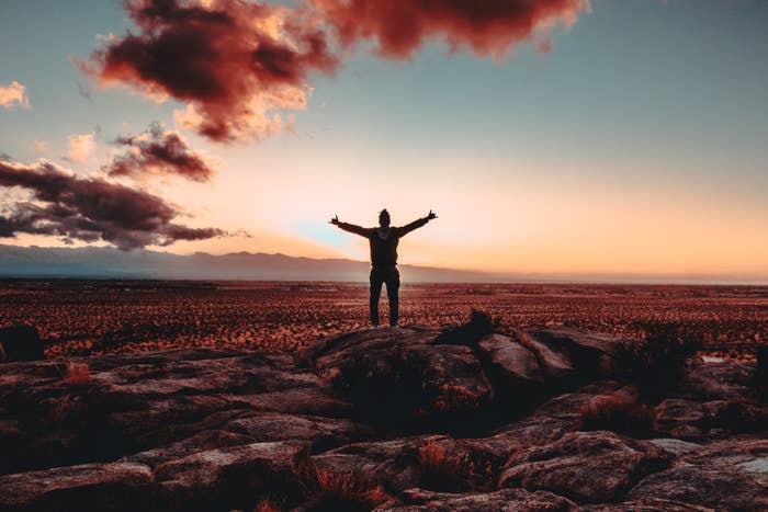 Person standing on a rock raising both hands to the sky