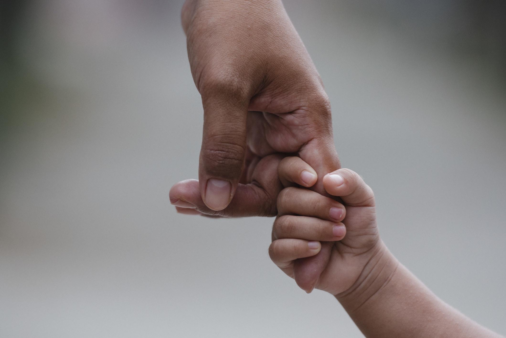 A child grips onto a parents hand tightly, not letting go