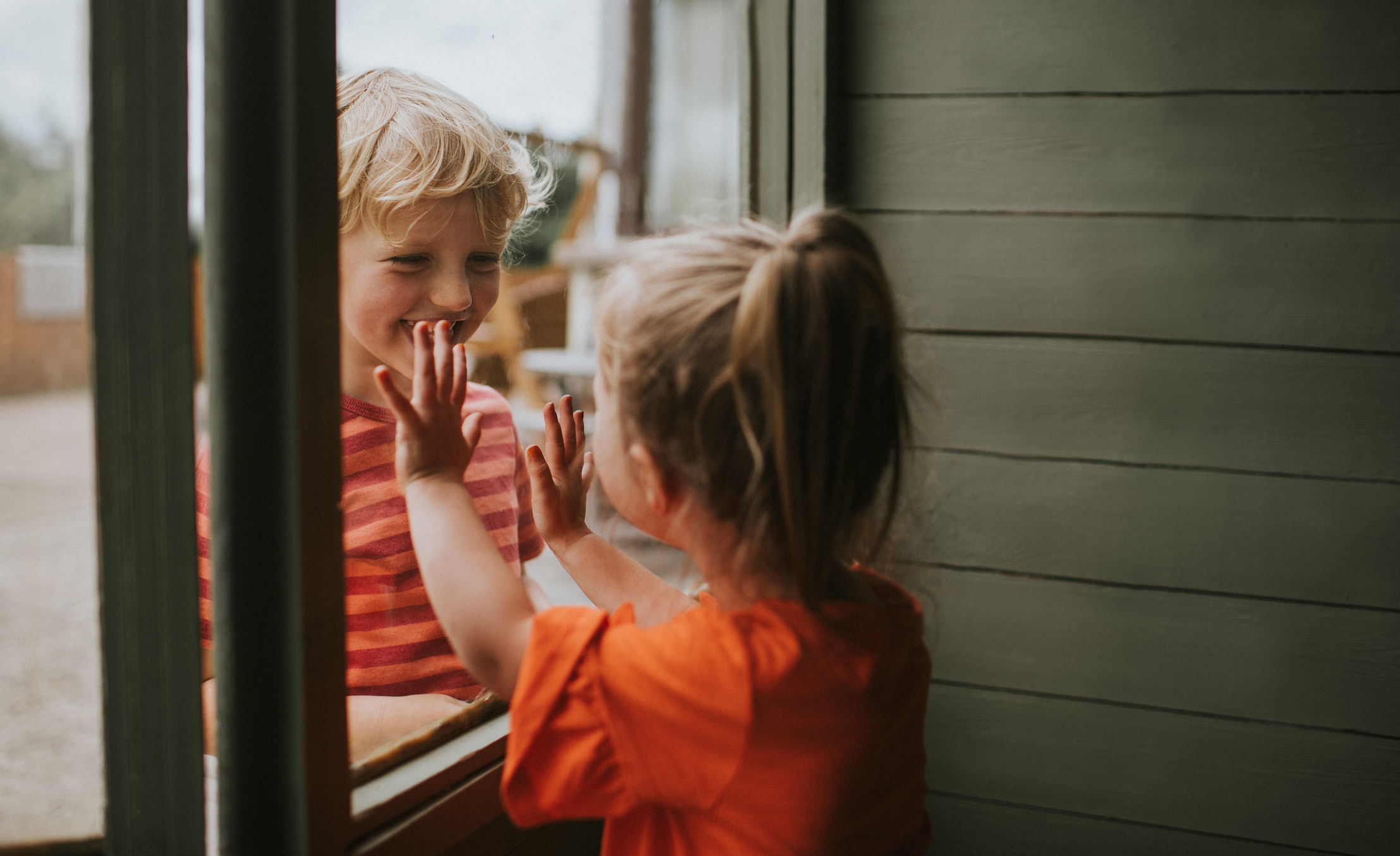 Two toddlers innocently smile at each other through a window