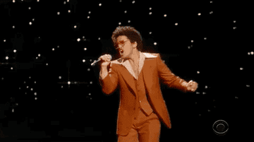 Bruno Mars singing into a mic in front of a sparkly background