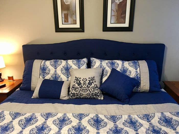 The blue tufted headboard with a slightly curved shape on a queen bed