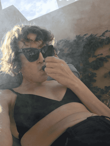 The author smokes out a pipe in their mother&#x27;s backyard while wearing a bikini top and jean shorts
